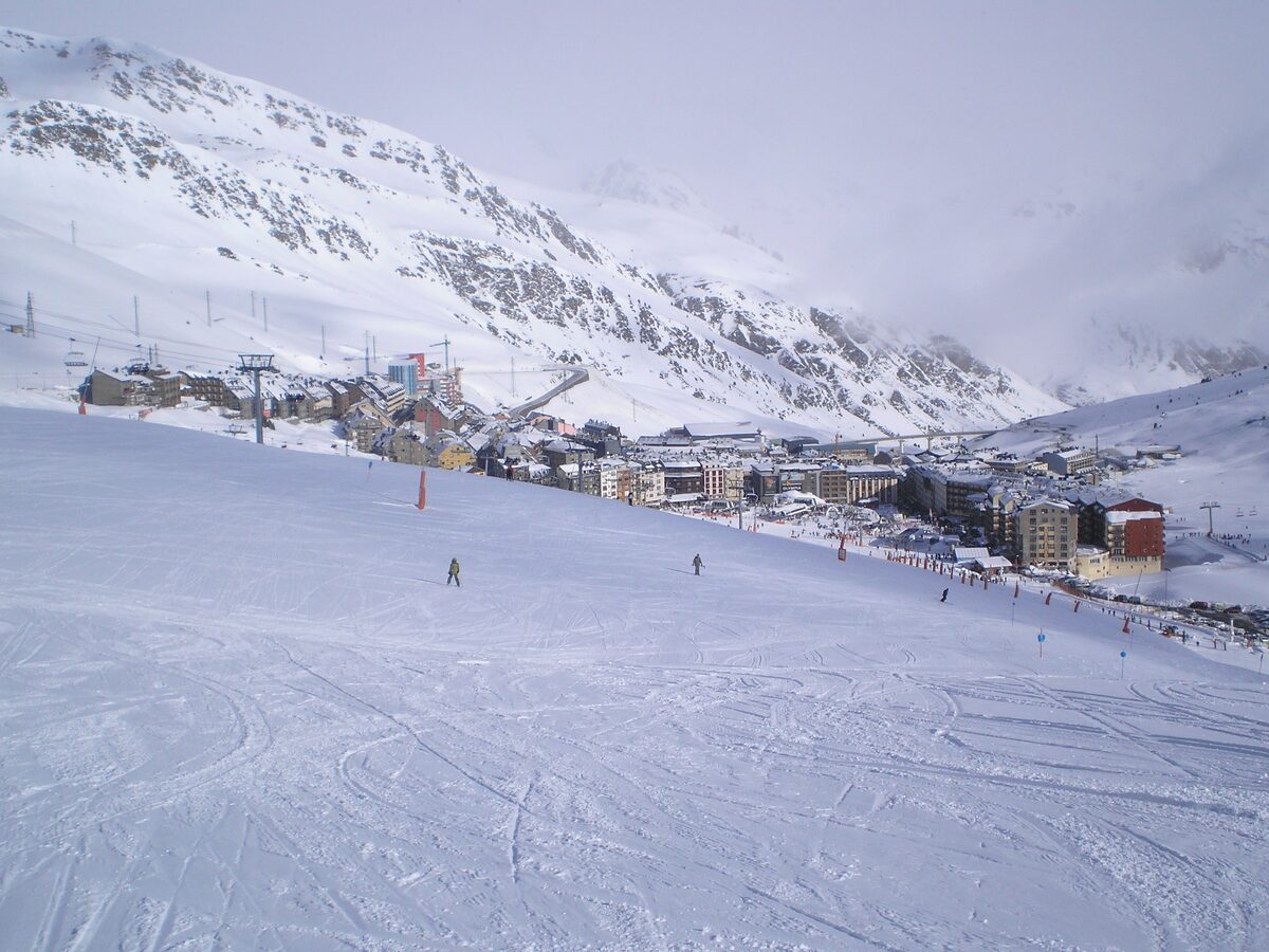 Pas de la Casa seen from the slopes above, with a skier on the piste, lifts and hotel blocks below snowy mountains