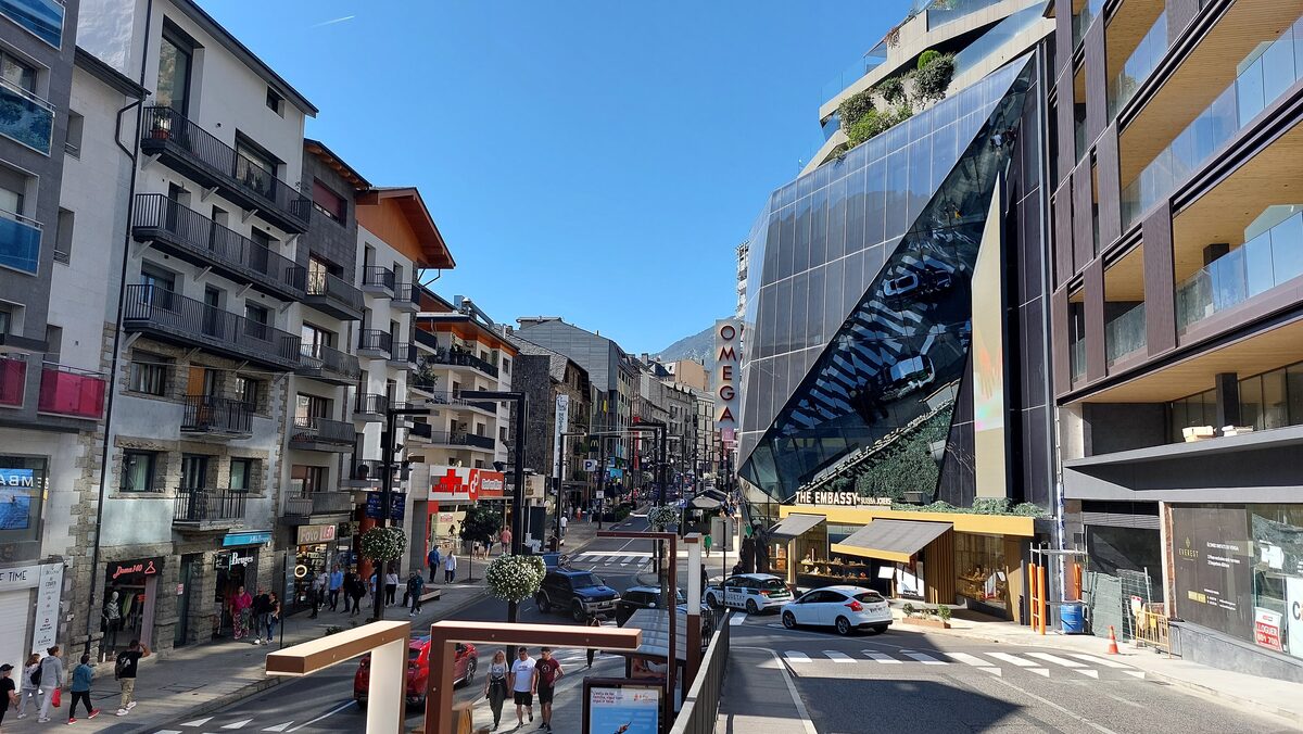 Avinguda Meritxell in Andorra la Vella, a sunny shopping street lined with shops and apartment blocks, mountains beyond