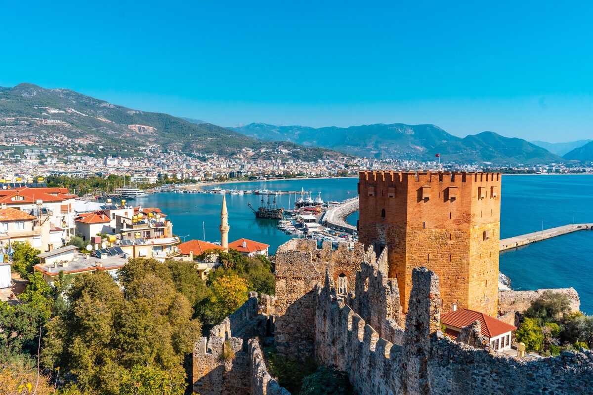 Alanya's octagonal Red Tower and castle walls above the harbor, with the city, the bay and mountains behind