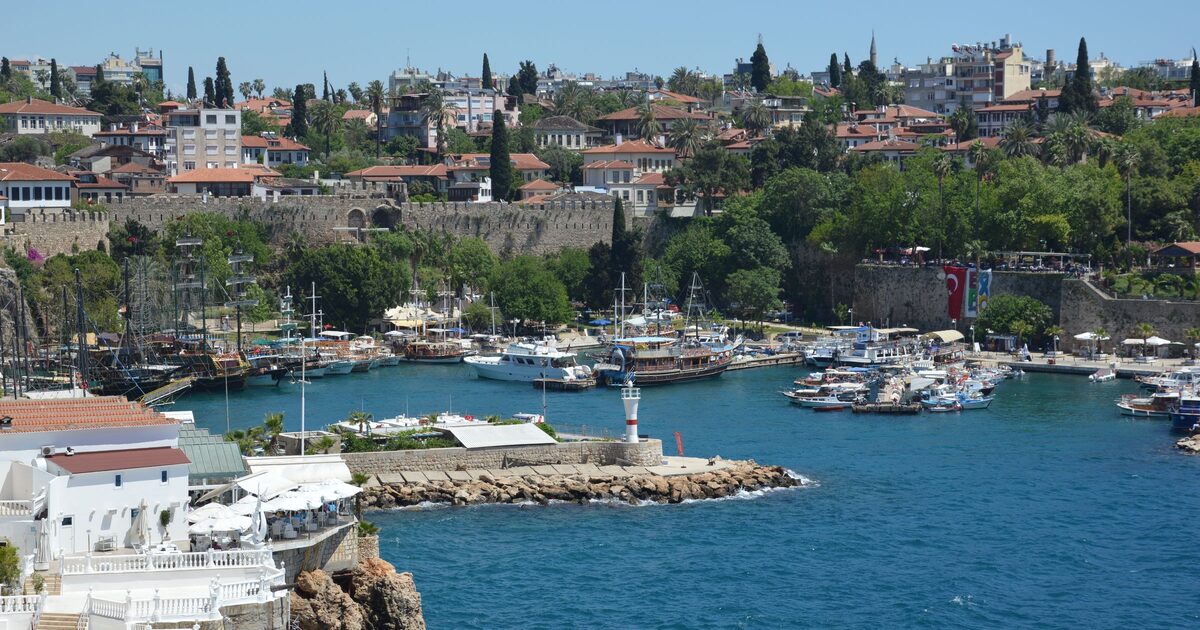 Kaleiçi's old harbor seen from the cliff, with gulets and boats, a small lighthouse on the breakwater, the old walls and red roofs above