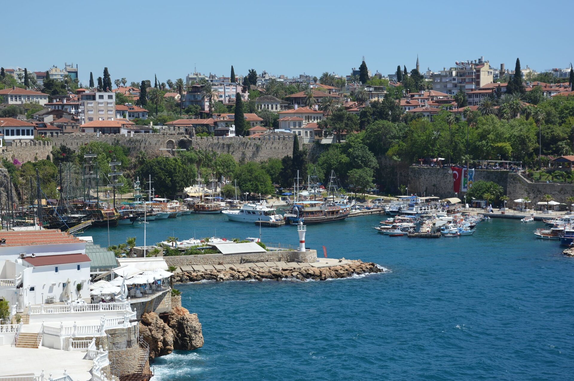 Kaleiçi's old harbor seen from the cliff, with gulets and boats, a small lighthouse on the breakwater, the old walls and red roofs above