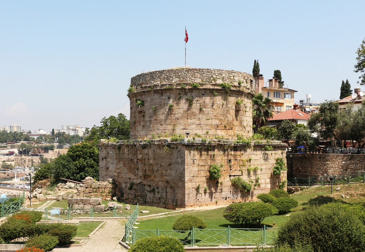 The round stone Hıdırlık Tower on its square base, with a Turkish flag on top, in a garden above the harbor