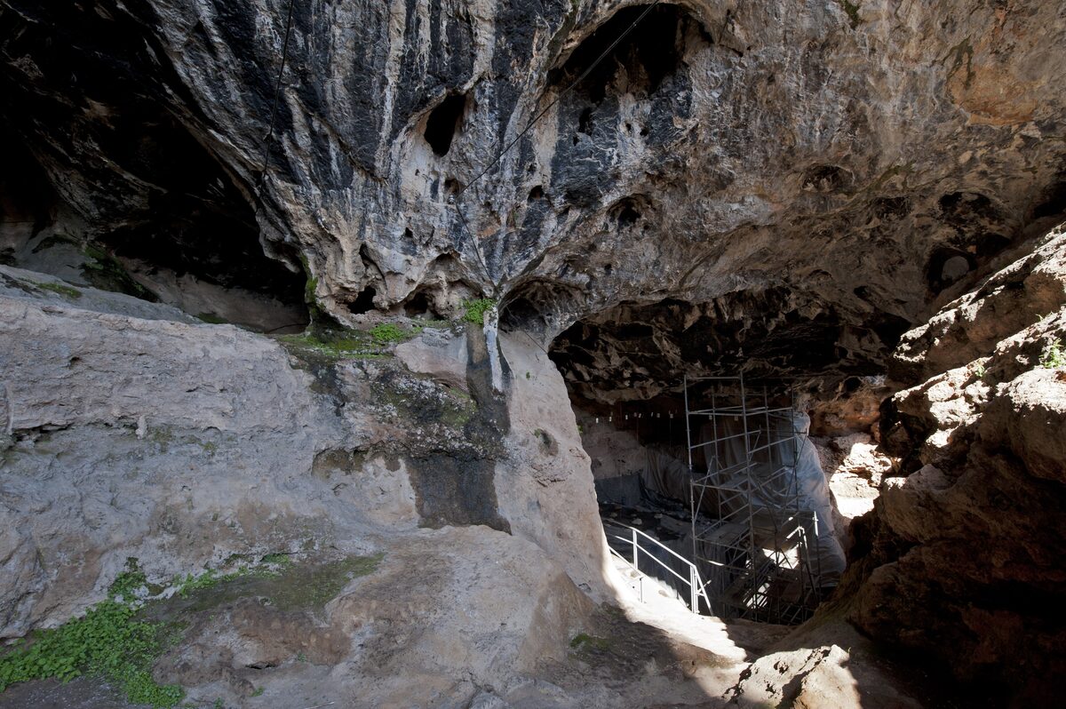 The mouth of Karain Cave under an overhanging limestone roof, with a walkway and excavation scaffolding inside