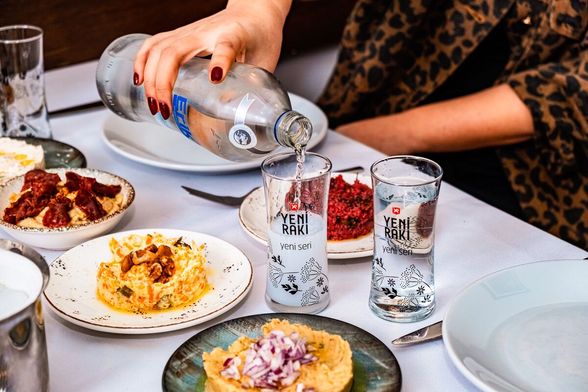 Rakı being poured into glasses over a table of meze