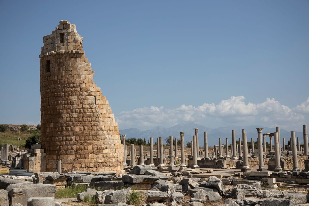 A ruined round Hellenistic gate tower at Perge beside rows of standing columns, with the Taurus Mountains behind