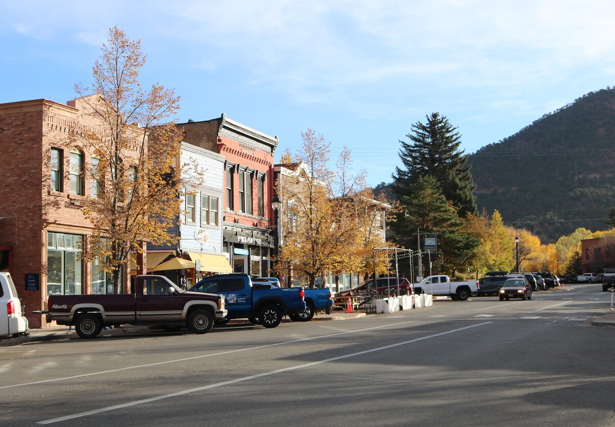 Brick storefronts along Midland Avenue in Basalt, with autumn trees and a wooded hill behind