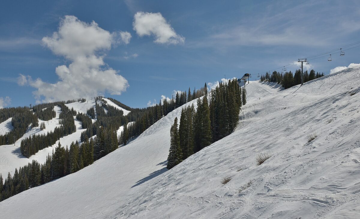 Groomed snow on a steep Aspen Mountain run below the Ajax Express chairlift, with fir trees along the ridge