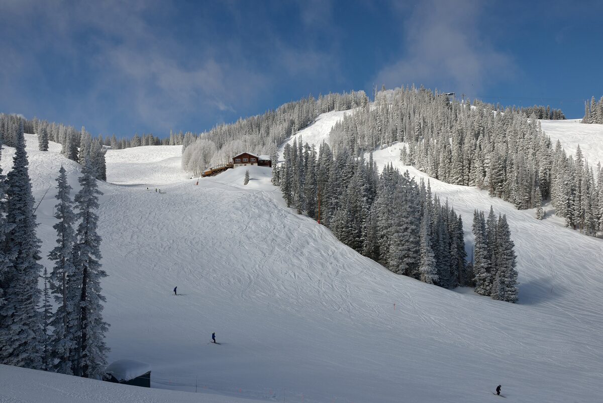 Skiers on the snowy runs of Aspen Mountain below Bonnie's, with frosted fir trees around the chalet