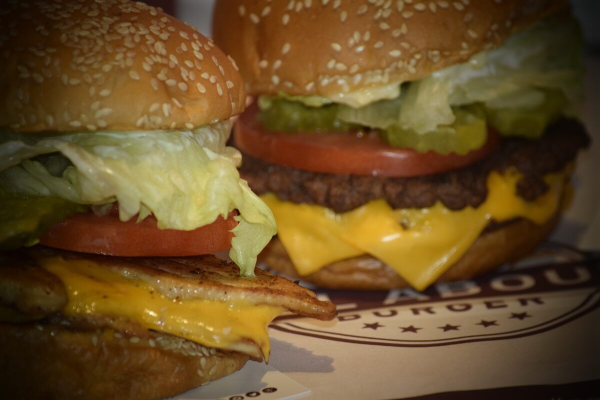 A double cheeseburger with lettuce, tomato, pickle and melted cheese on a paper wrapper