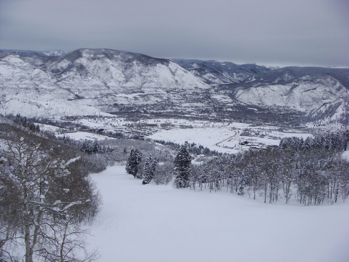 Snow-covered slopes above a wide valley and a small town, seen from the Buttermilk runs