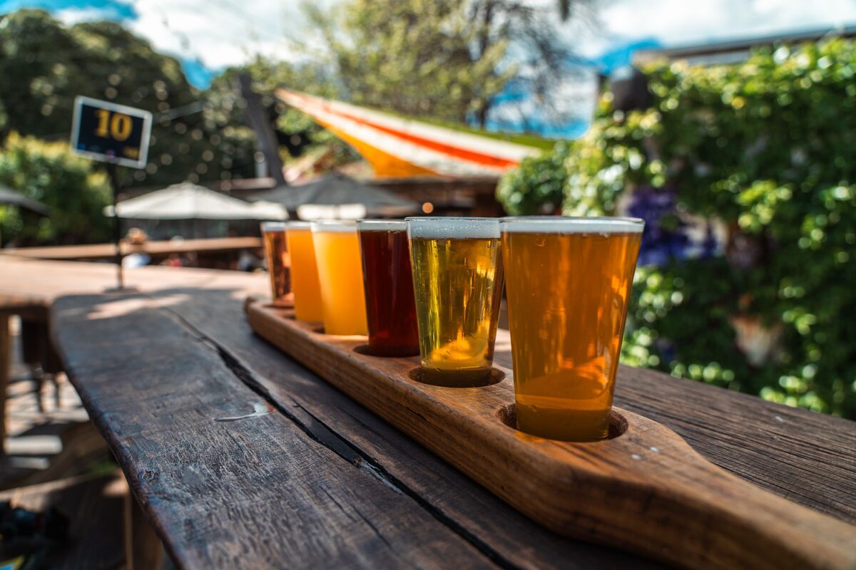 A wooden paddle holding a flight of five craft beers on an outdoor table