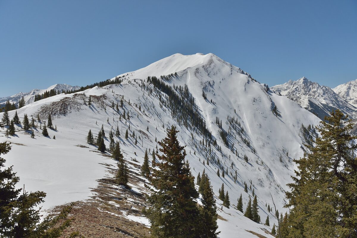 Highland Peak at Aspen Highlands, a snow-covered ridge and summit with fir trees in the foreground
