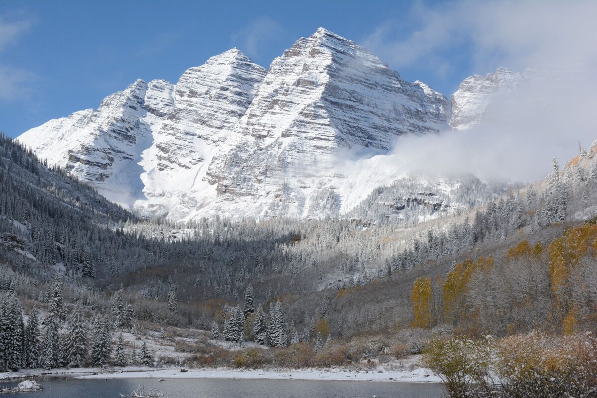 The Maroon Bells under early-season snow above Maroon Lake, with a few golden aspen leaves still on the valley side