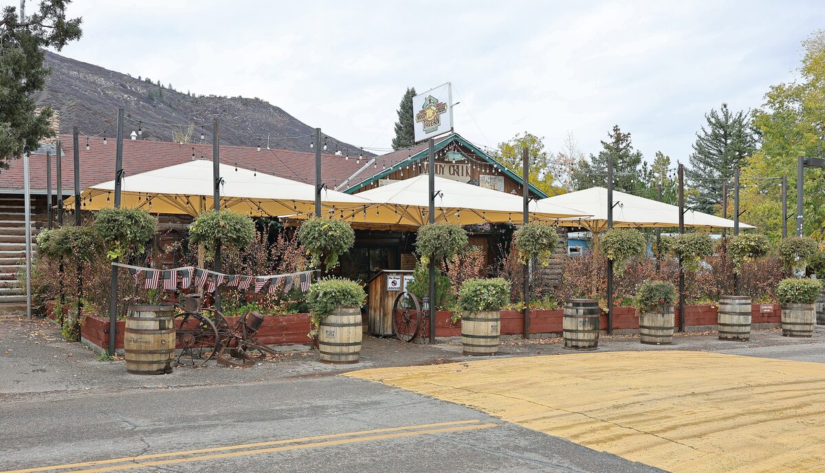 The front of Woody Creek Tavern, with a shaded patio, planters and barrels, on an autumn day