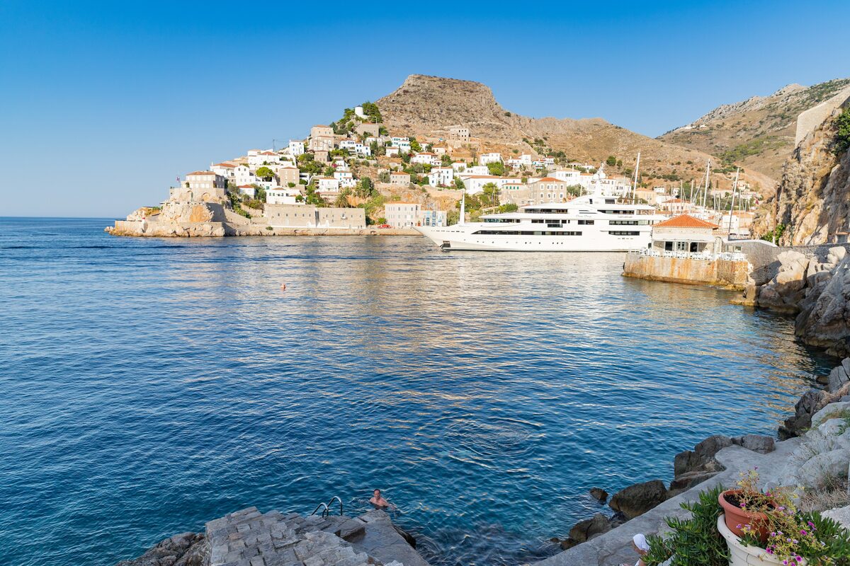 Clear blue water at the swimming rocks below Hydra town, with the harbor houses across the bay