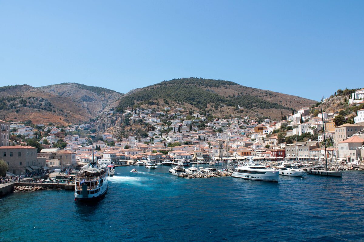 Hydra harbor from the sea, with a ferry and yachts in front of stone mansions climbing the bare hills