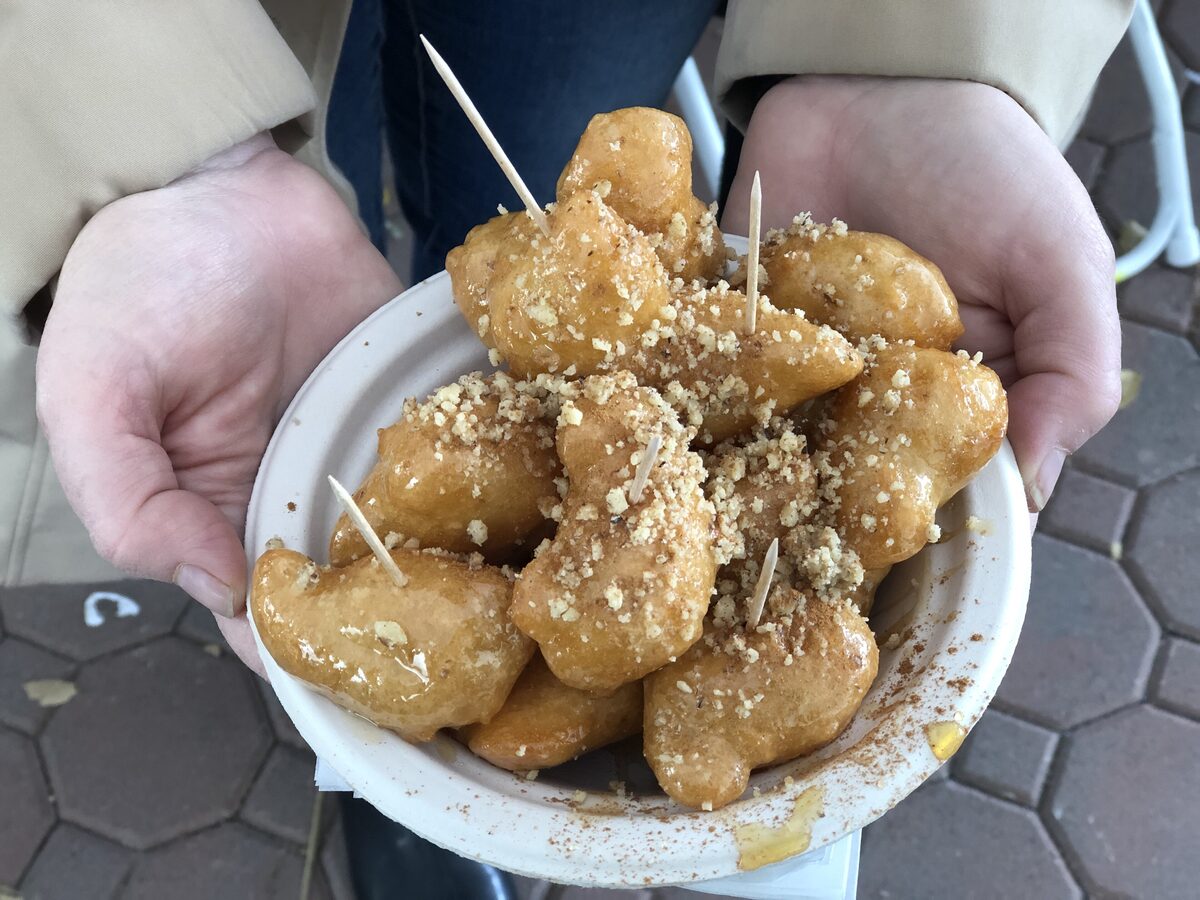 A paper bowl of honey-soaked loukoumades sprinkled with chopped walnuts