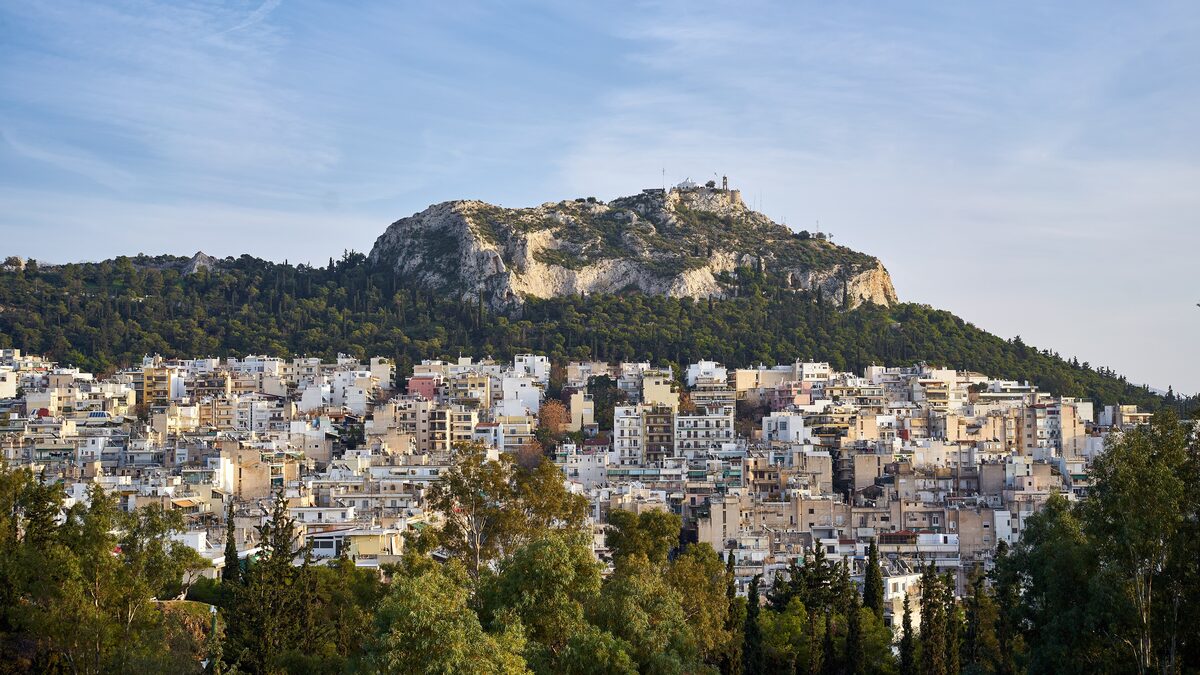 Lycabettus Hill in evening light, its rocky summit and chapel above pine slopes and the white apartment blocks of Kolonaki