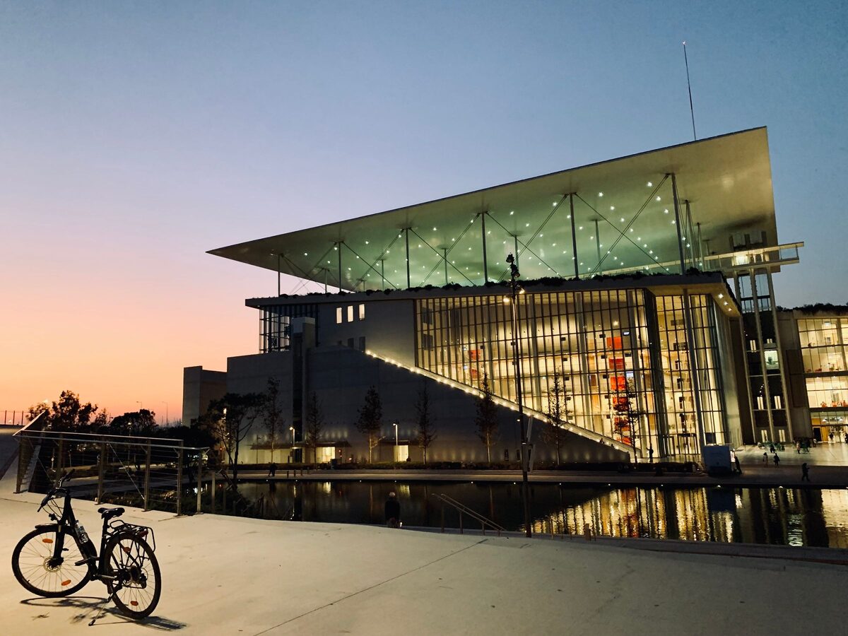 The Stavros Niarchos Foundation Cultural Center at dusk, its glass front lit under the floating solar canopy