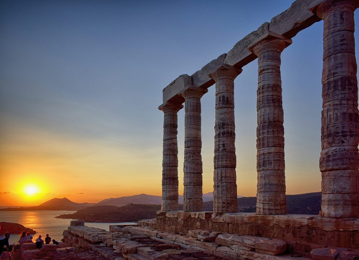 The columns of the Temple of Poseidon at Cape Sounion against an orange sunset over the sea