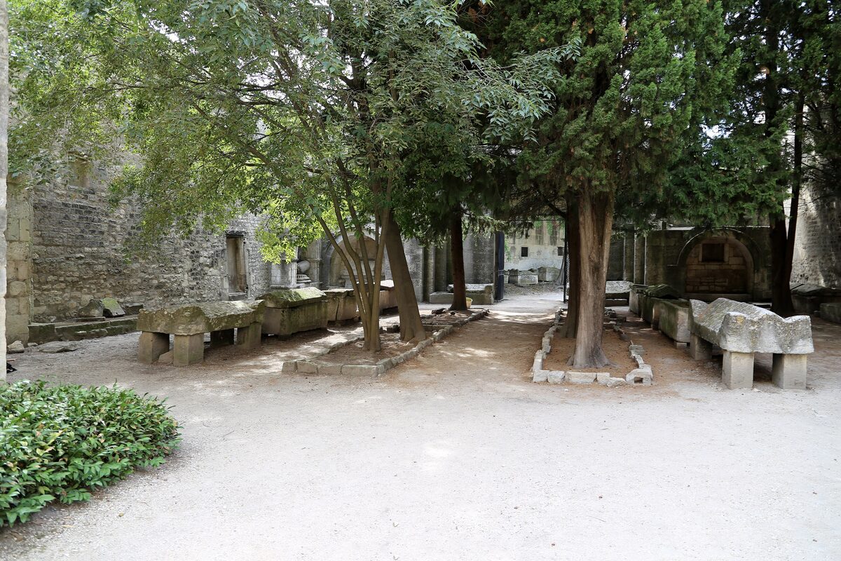Old stone sarcophagi standing among trees on the gravel of the Alyscamps burial ground in Arles