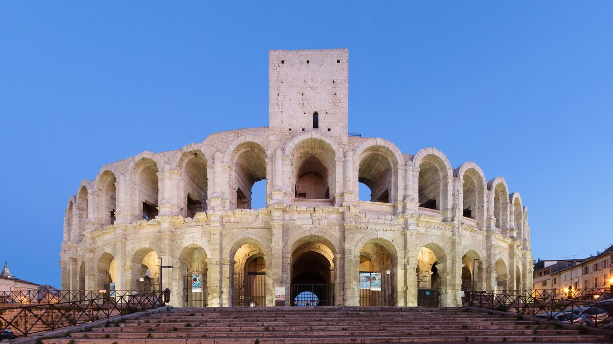 The Roman arena of Arles lit up at blue hour, with its tiers of arches and a tower on top