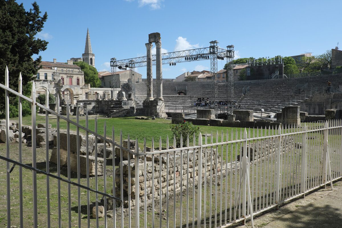 The stage columns and tiered seats of the Roman theatre in Arles, with a metal stage rig and trees behind