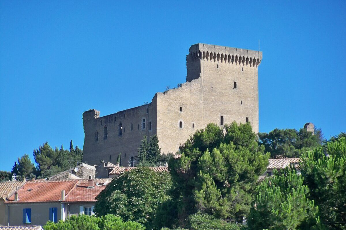 The crenellated stone tower and walls of the castle of Châteauneuf-du-Pape above pine trees and village roofs, under a clear blue sky