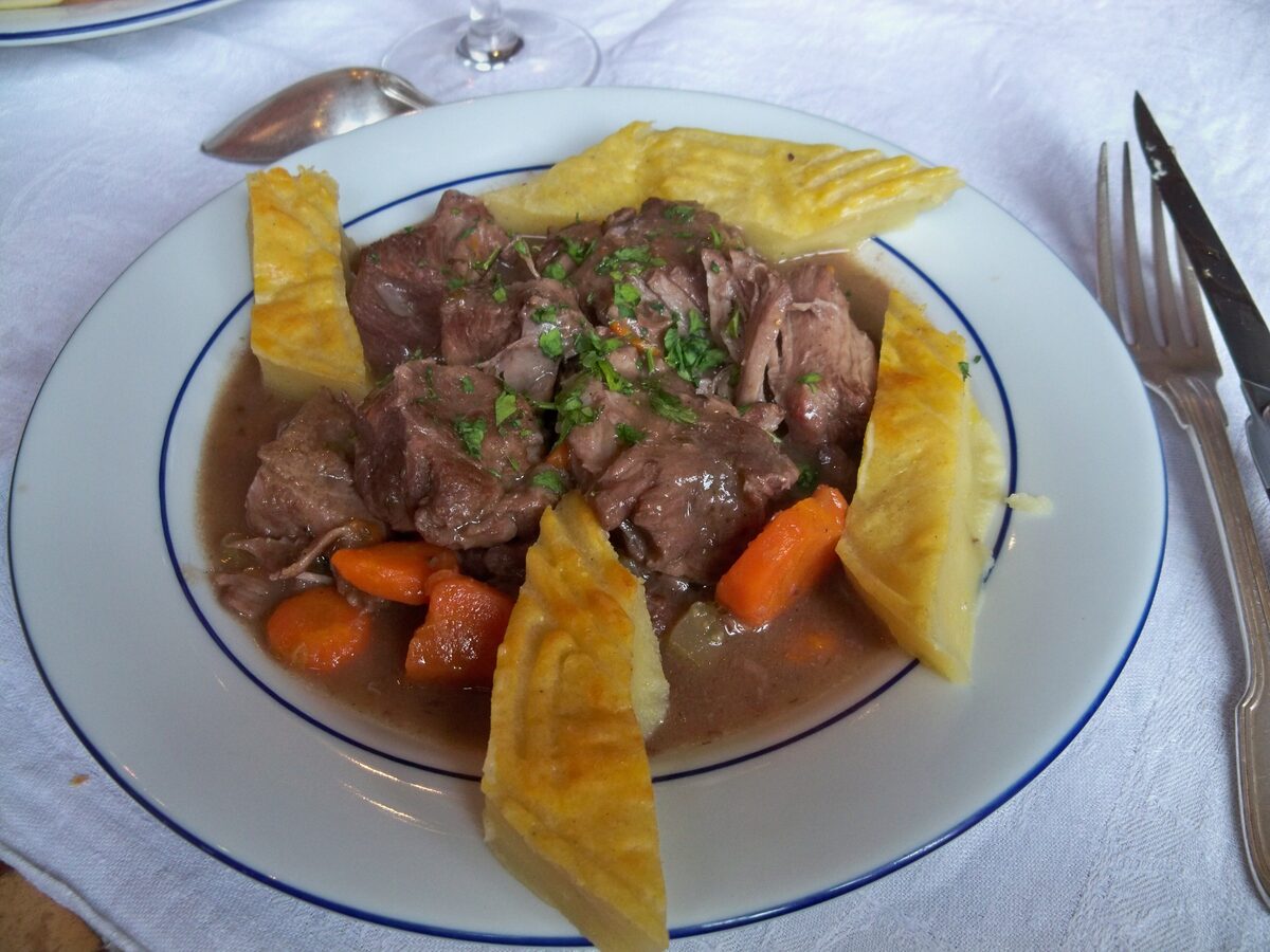 Beef daube in red-wine sauce with carrots, served with golden baked wedges on a white plate