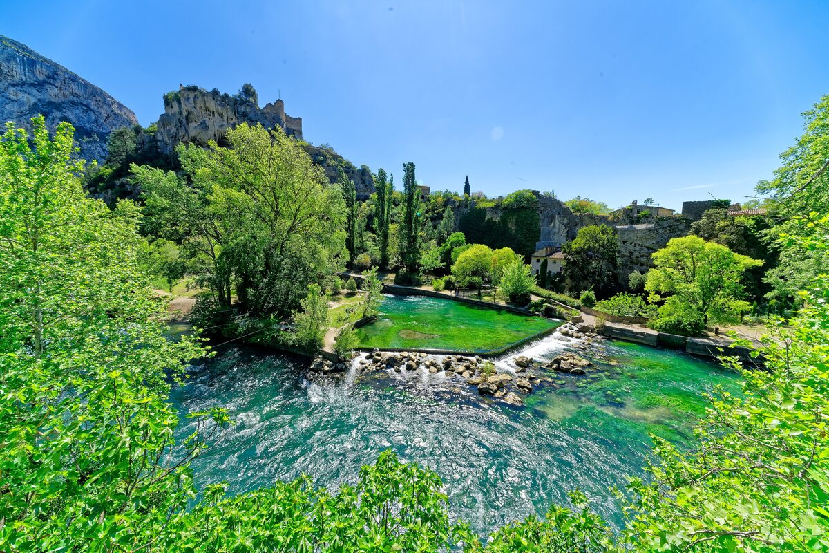 The clear green-blue pool of the Sorgue spring at Fontaine-de-Vaucluse, with rocks and trees around it