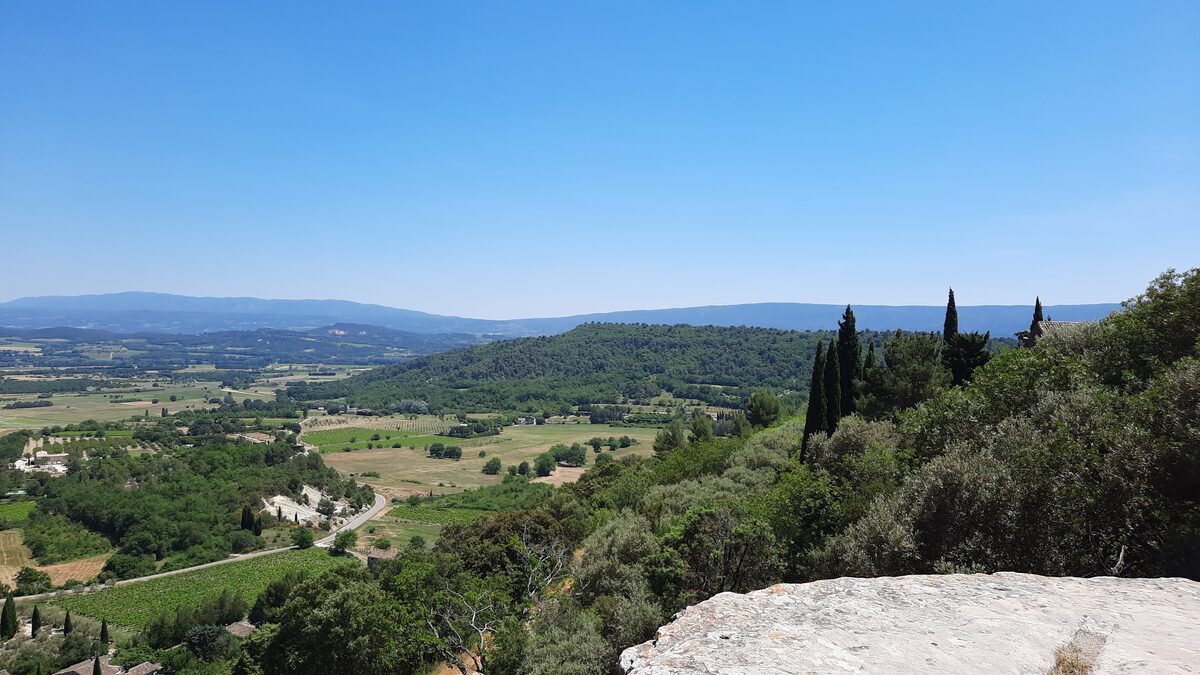 The valley around Gordes from a hillside, with cypress trees, fields and the Luberon hills in the distance