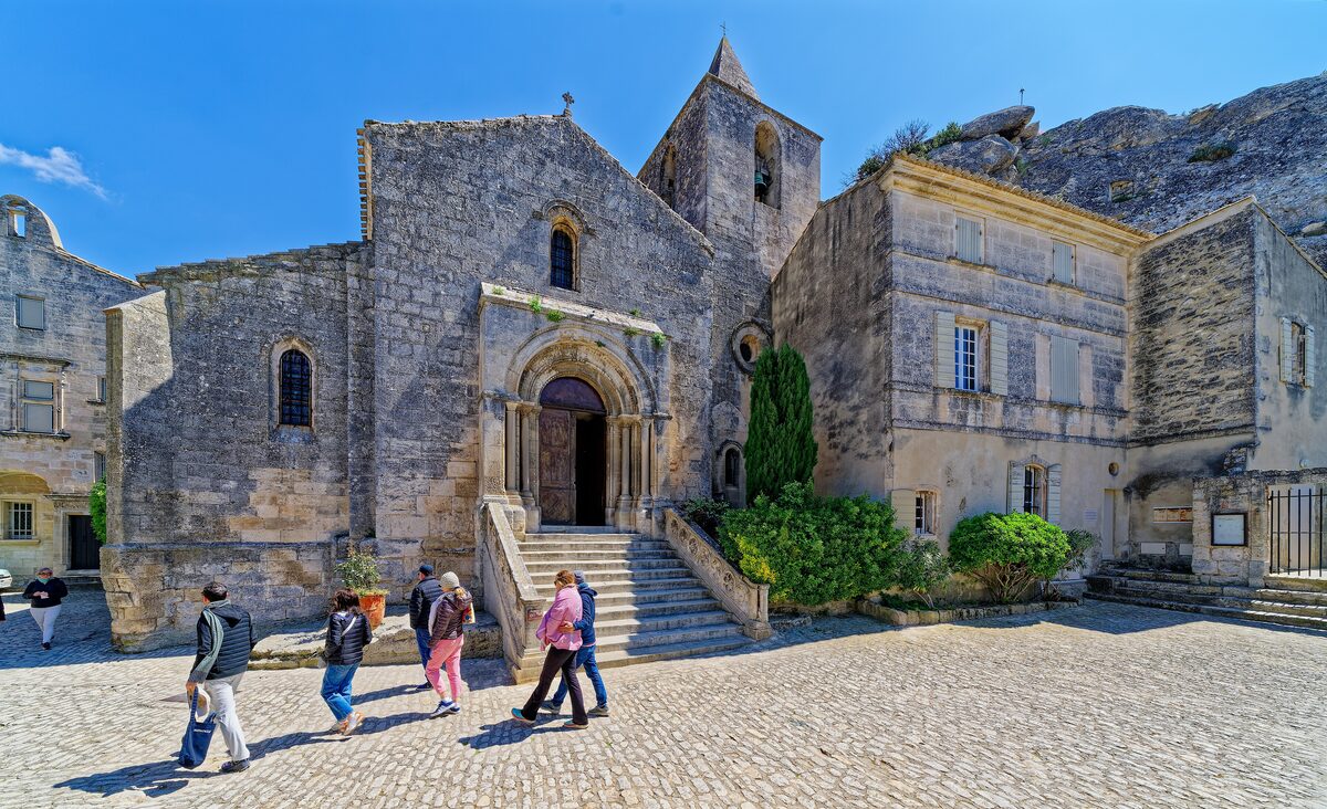 The church and cobbled square of Les Baux-de-Provence, with visitors crossing the square in front of the steps