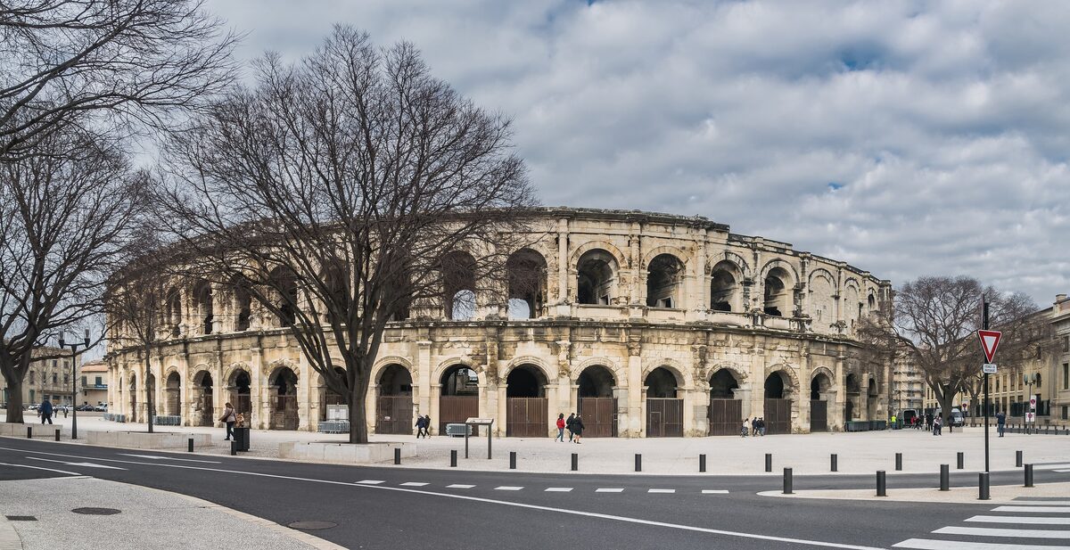 The Arènes de Nîmes, a Roman amphitheatre, seen from the street under a grey winter sky