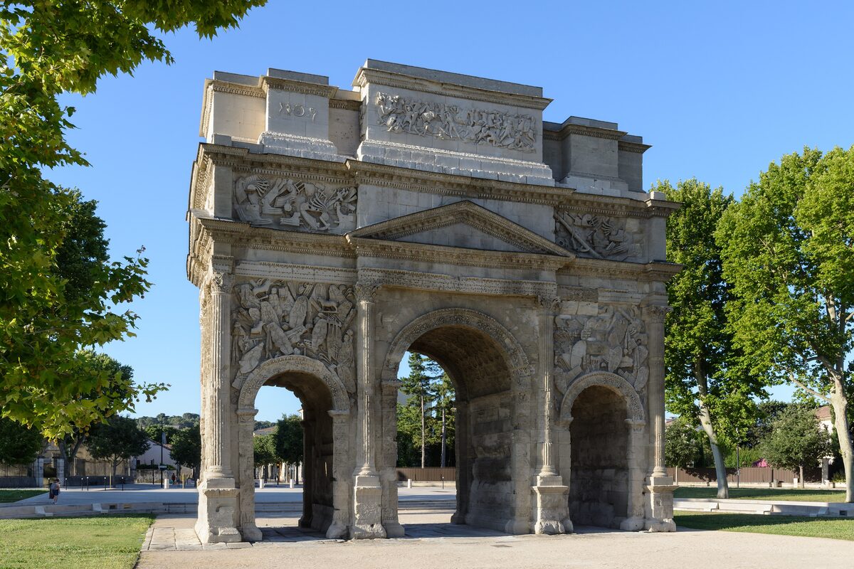 The Triumphal Arch of Orange, with its three archways and carved reliefs, under a clear blue sky