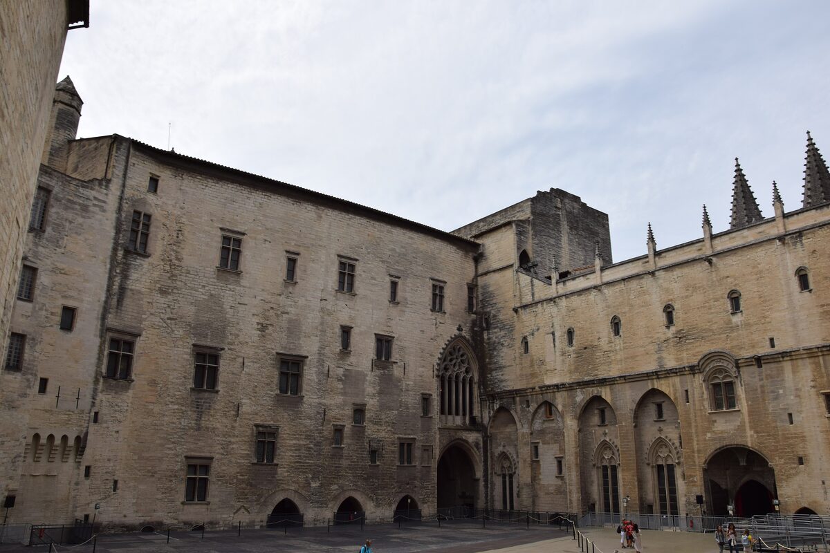 The Gothic courtyard facade of the Palais des Papes, with pointed windows, arched doorways and pale stone walls