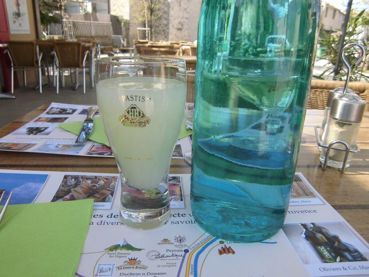 A glass of pale pastis beside a blue-green bottle of water on a café table