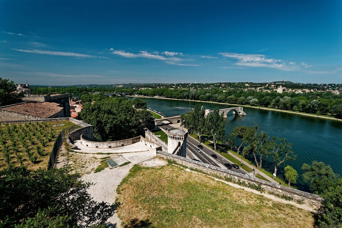 View from the Rocher des Doms gardens over the Rhône, with the ramparts and the broken arches of the Pont Saint-Bénézet under a blue sky