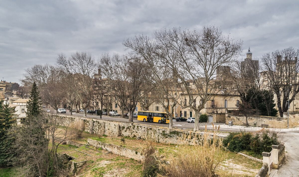 Uzès seen from the river side, with a row of trees and a yellow bus in front of the old town