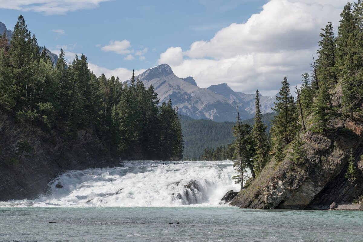 Bow Falls spilling over a low ledge with forested mountains behind