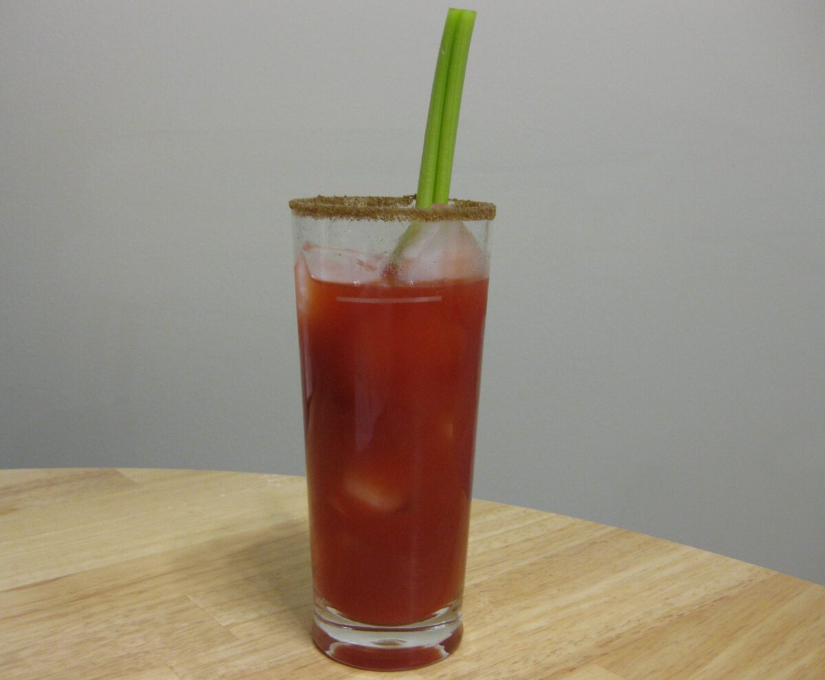 A tall Caesar cocktail with a celery stick and spiced rim