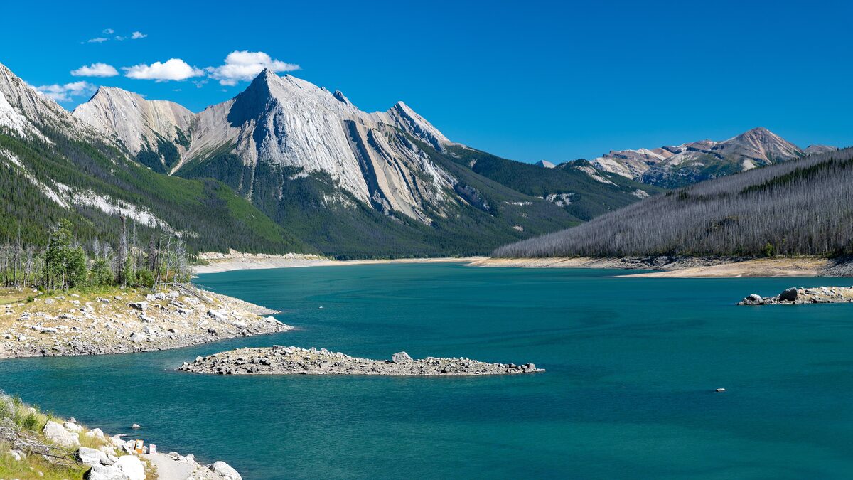 Medicine Lake's green water and sharp peaks under a clear blue sky