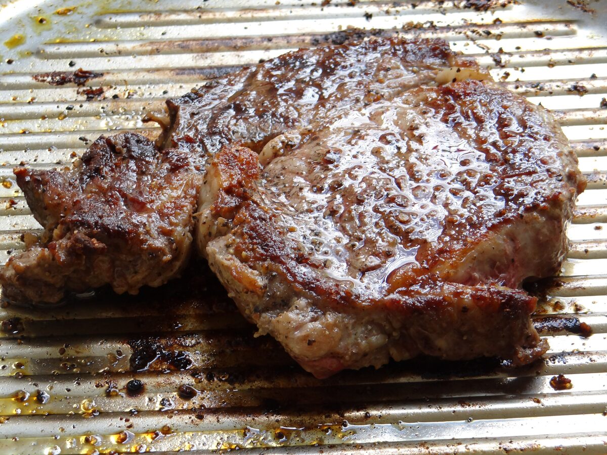 A thick, well-seared rib-eye steak with a browned crust, resting on a grooved cooking surface