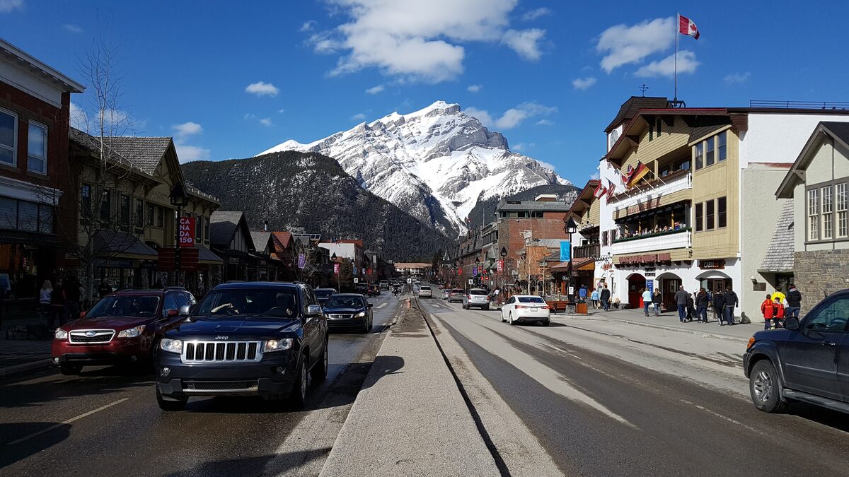 Banff Avenue running toward snow-capped Cascade Mountain, with traffic and mountain-style buildings on both sides