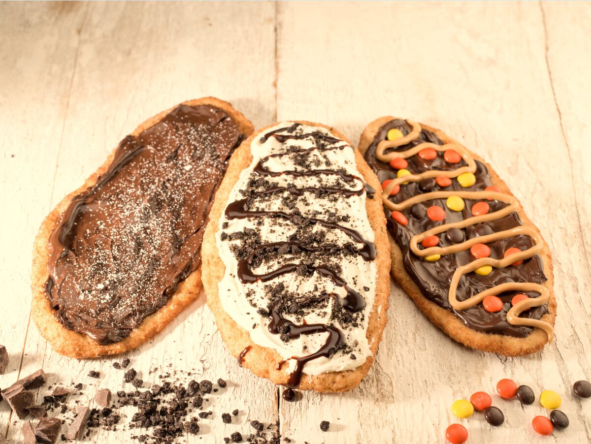 Three oval BeaverTails pastries topped with chocolate hazelnut spread, cookie crumbs, peanut butter drizzle and candy pieces