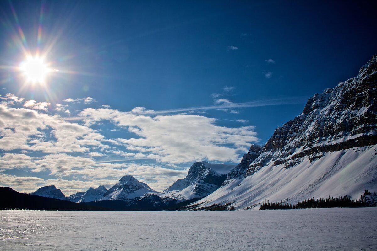 Frozen, snow-covered Bow Lake under a bright winter sun with the Crowfoot massif rising on the right