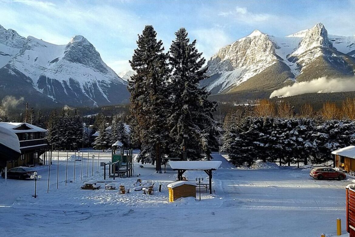 A snowy Canmore street scene with jagged, snow-dusted Bow Valley peaks rising above the spruce trees