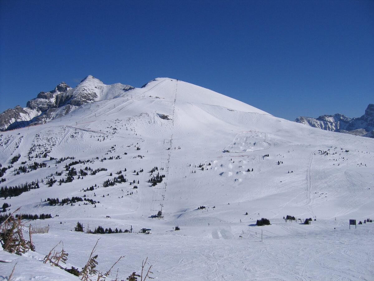 A wide snowy ridge above Sunshine Village with ski tracks running down toward the Continental Divide under a deep blue sky