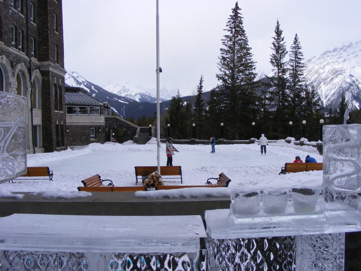 Skaters on a small rink in the snow beside the Fairmont Banff Springs, with ice sculptures and mountains behind
