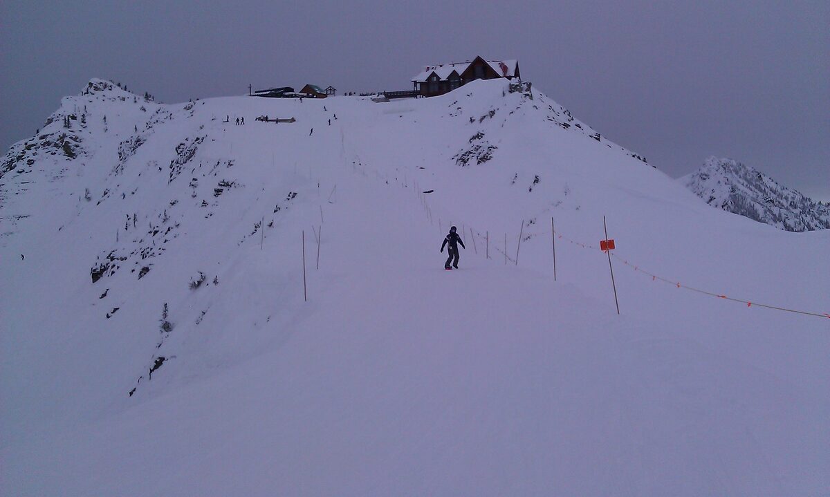 A lone skier on a snowy ridge below the summit lodge at Kicking Horse Mountain Resort