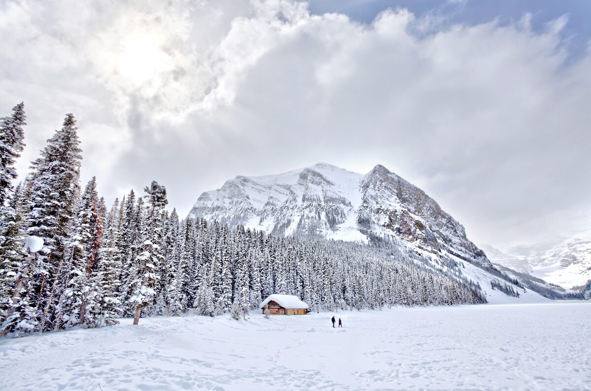 Frozen Lake Louise under snow, with a small cabin among frosted spruce and a mountain rising behind